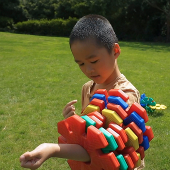 Ein kleiner Junge spielt auf einer Rasenfläche mit einer farbenfrohen Konstruktion aus Giant Octoplay-Scheiben